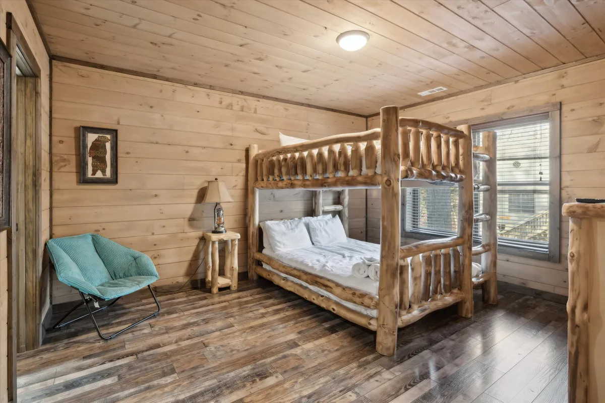 A cozy bedroom featuring a wooden bunk bed, blue chair, and warm lighting from a lamp. Wooden furniture and a shared space evoke a family-friendly environment, while the inviting setup is ideal for children or friends traveling together. The room balances comfort and functionality, supporting flexible sleeping arrangements.