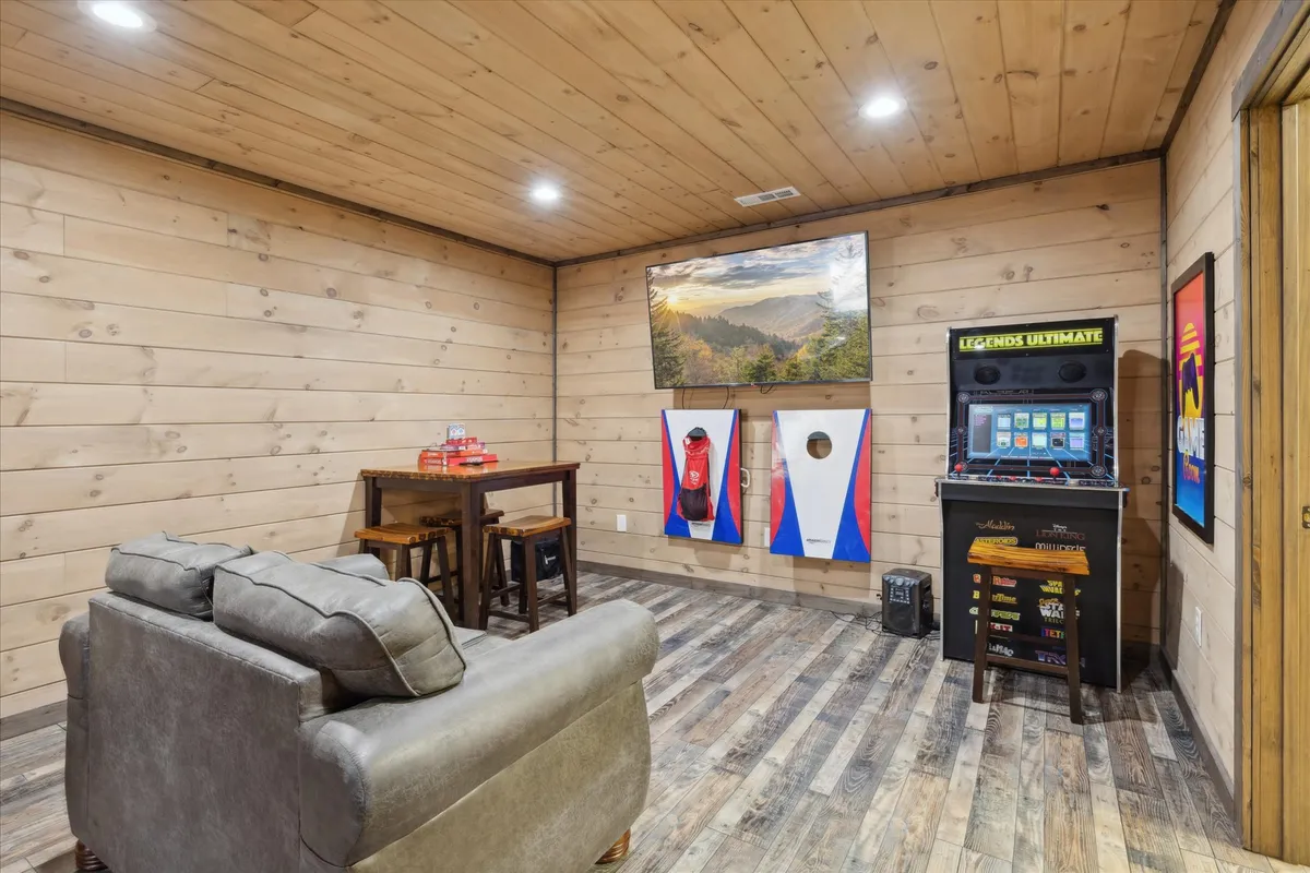 This image captures an open-concept living space featuring a sofa, a dining table with chairs, and an arcade machine. The wall art and cozy furnishings create a playful yet relaxed mood, perfectly suited for gatherings, gaming, and movie nights. The space feels communal and welcoming, with clear sightlines to different activity zones.
