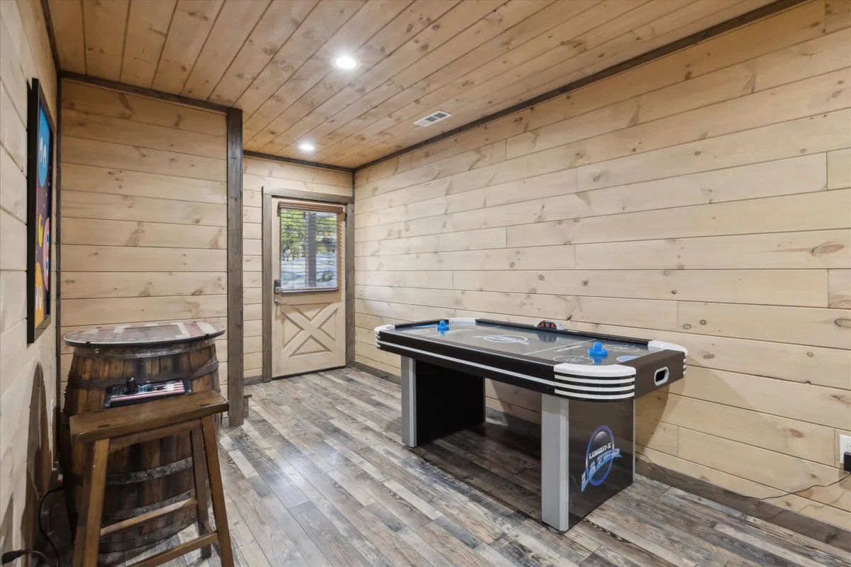 This image focuses on a lively game room featuring an air hockey table, a wooden barrel table, and an exterior door leading outside. The space is set up for friendly competitions and group fun, capturing the energy of social gatherings and interactive play.