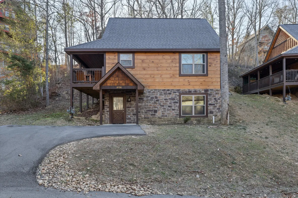 The image showcases the inviting wooden exterior of the cabin, set atop a sturdy stone foundation, with a welcoming front porch—the perfect spot to soak in golden sunset views. The cozy setting is enhanced by hints of family-friendly outdoor spaces and the natural beauty of the Smoky Mountains.