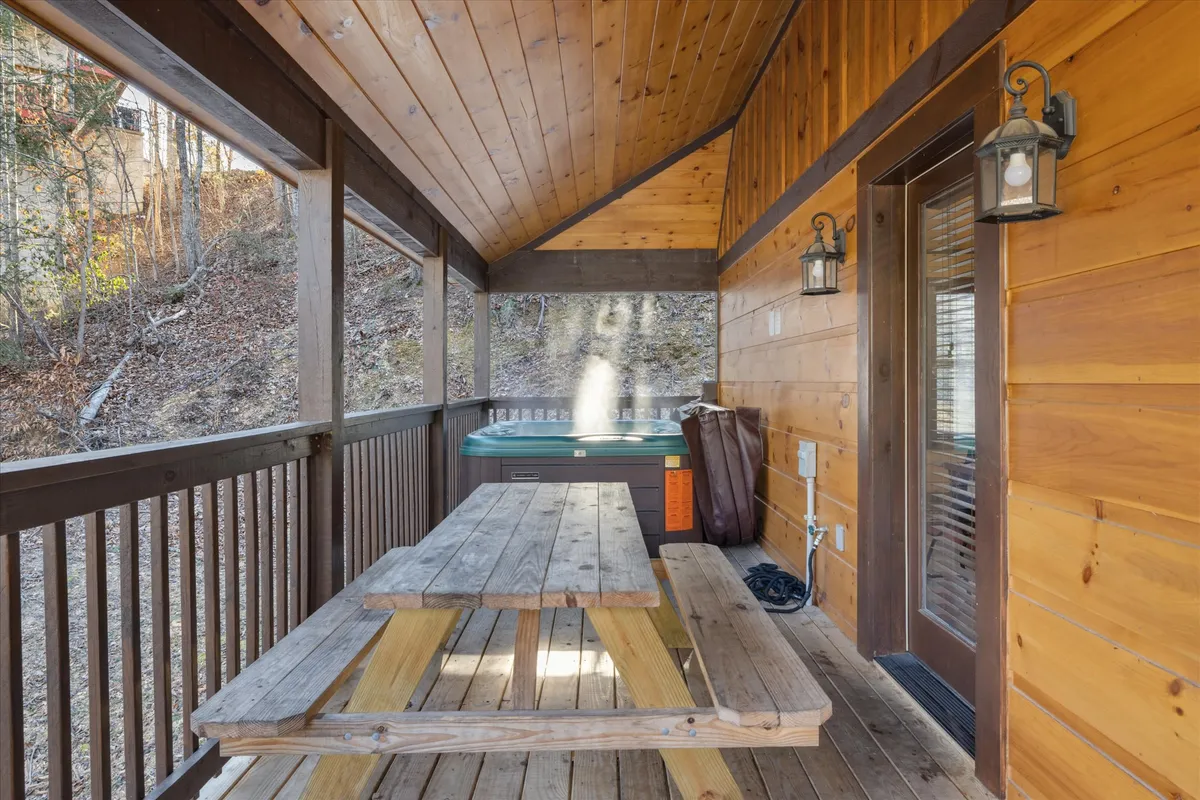 An exterior view showcasing the hot tub situated on a covered porch, with a wooden picnic table nearby and sunset views visible in the background. The scene blends the pleasures of outdoor soaking and dining, all set against a cozy, natural backdrop.