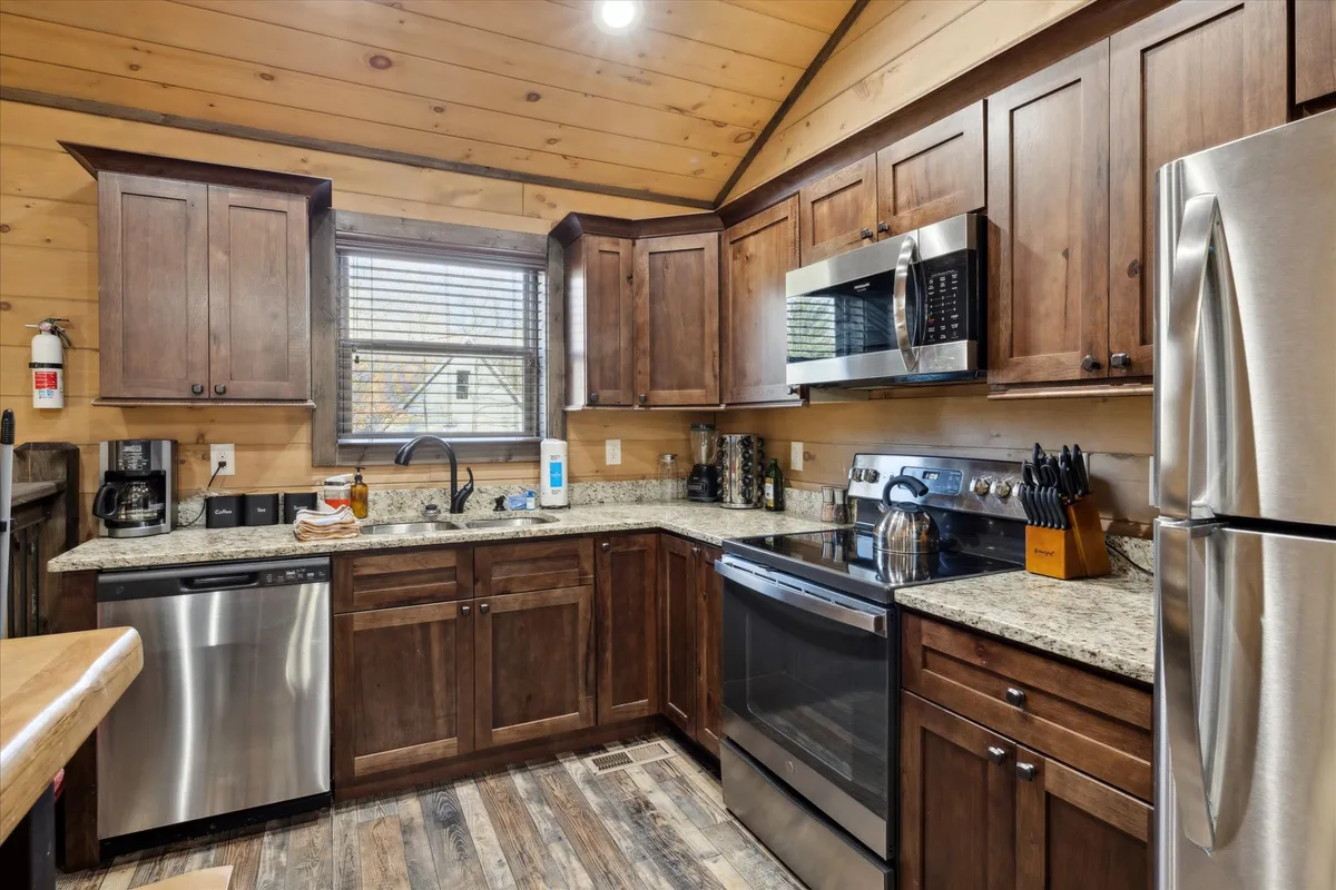 A close-up of a granite countertop with dark wooden cabinets and stainless steel appliances, set next to a window with blinds. The scene is cozy and inviting, hinting at morning routines or meal preparation.